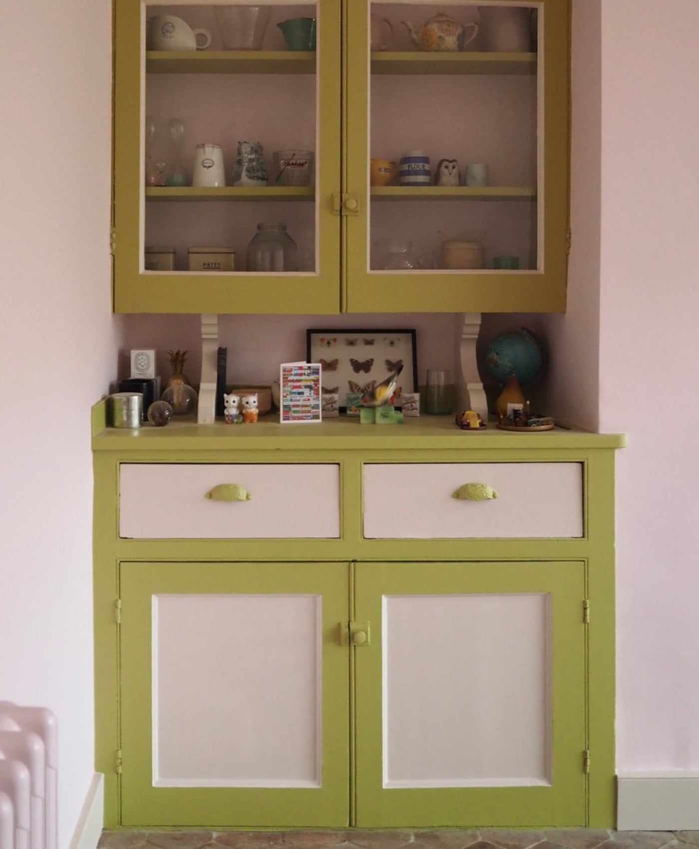 Lime green cabinet with glass doors and white drawers against a pink wall.