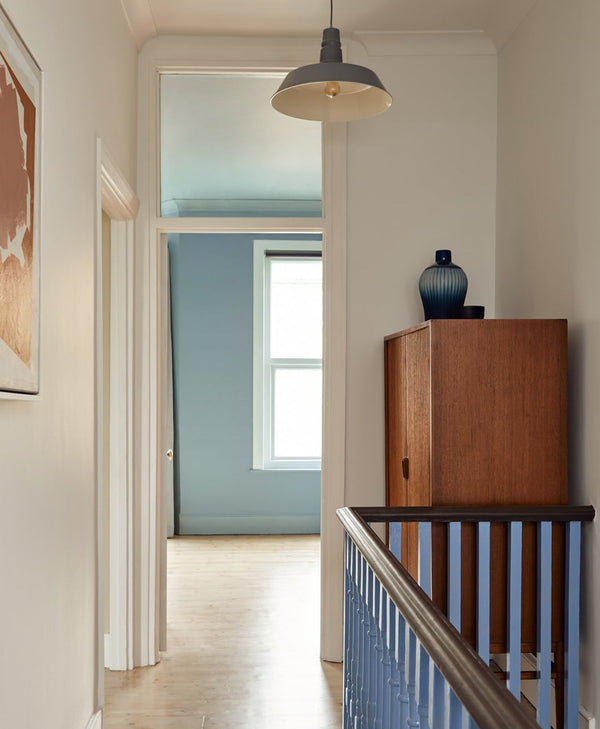 Narrow white hallway with wooden cabinet, mirror, and light fixture. Leading to classic blue room.