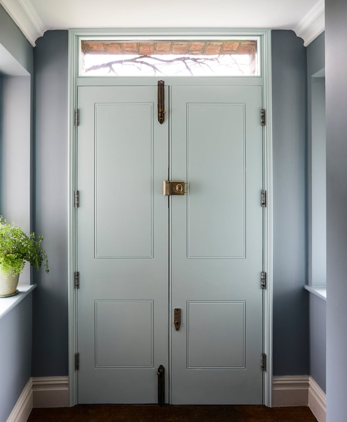 Pair of blue grey doors with brass hardware in a room with costal grey walls and a small window above the doors.
