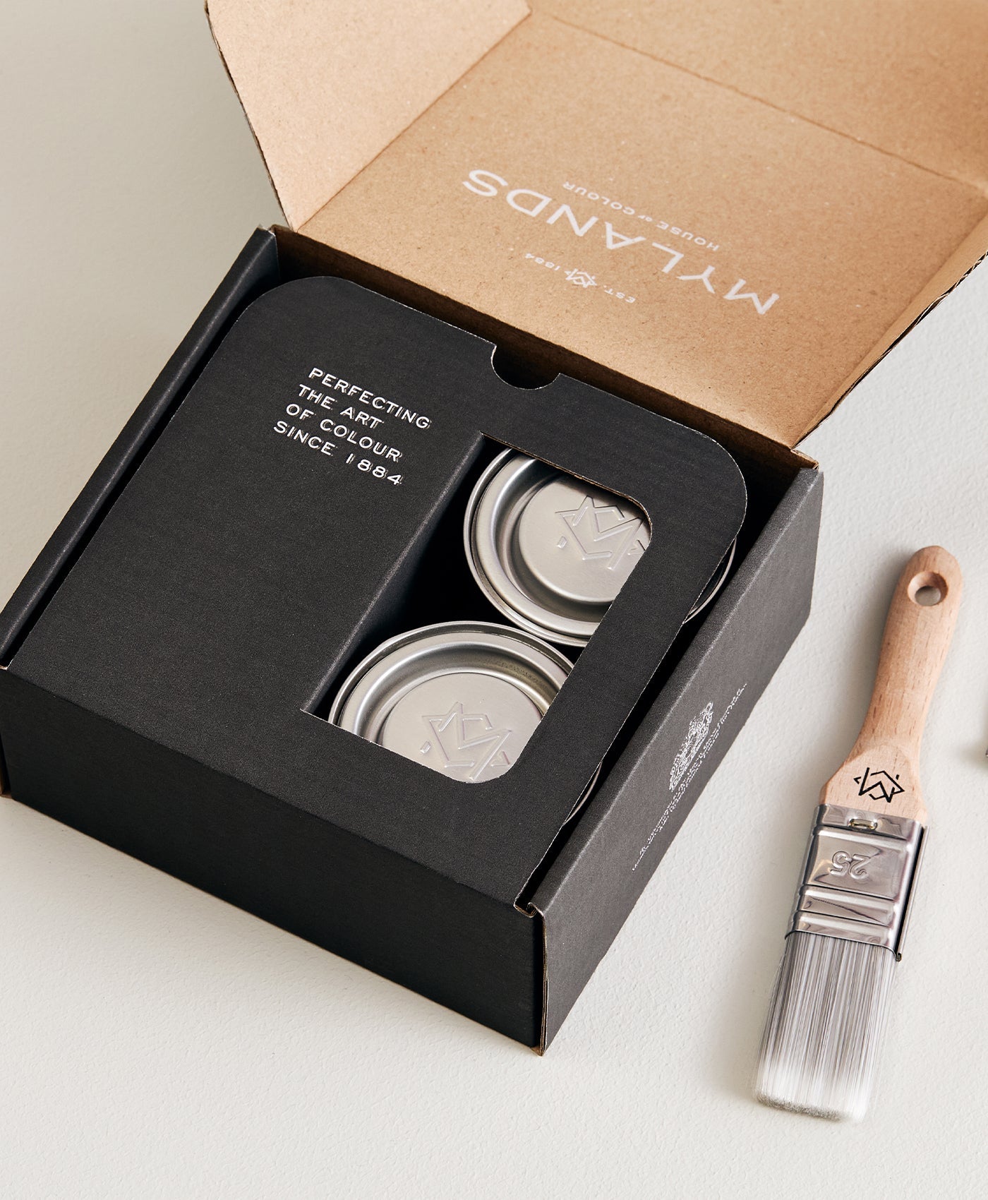 Mylands paint samples set of 4 - in a black box with a brush on a light surface, featuring the brand 'Mylands'.