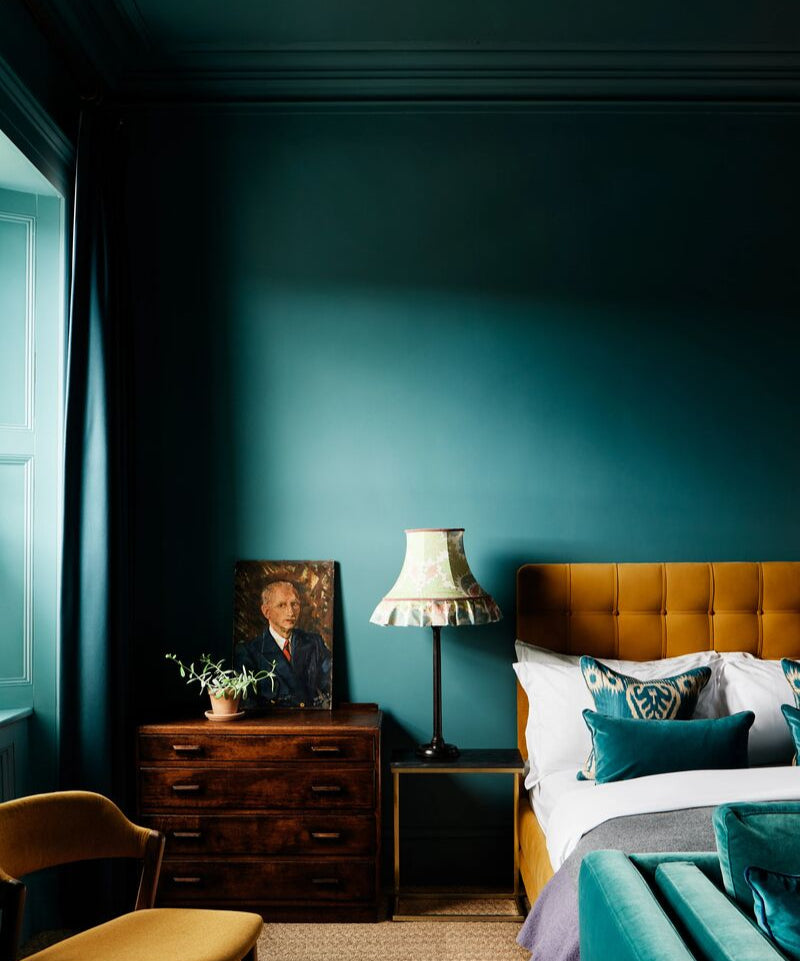 Cosy bedroom with teal walls, wooden furniture, and a brown upholstered bed.
