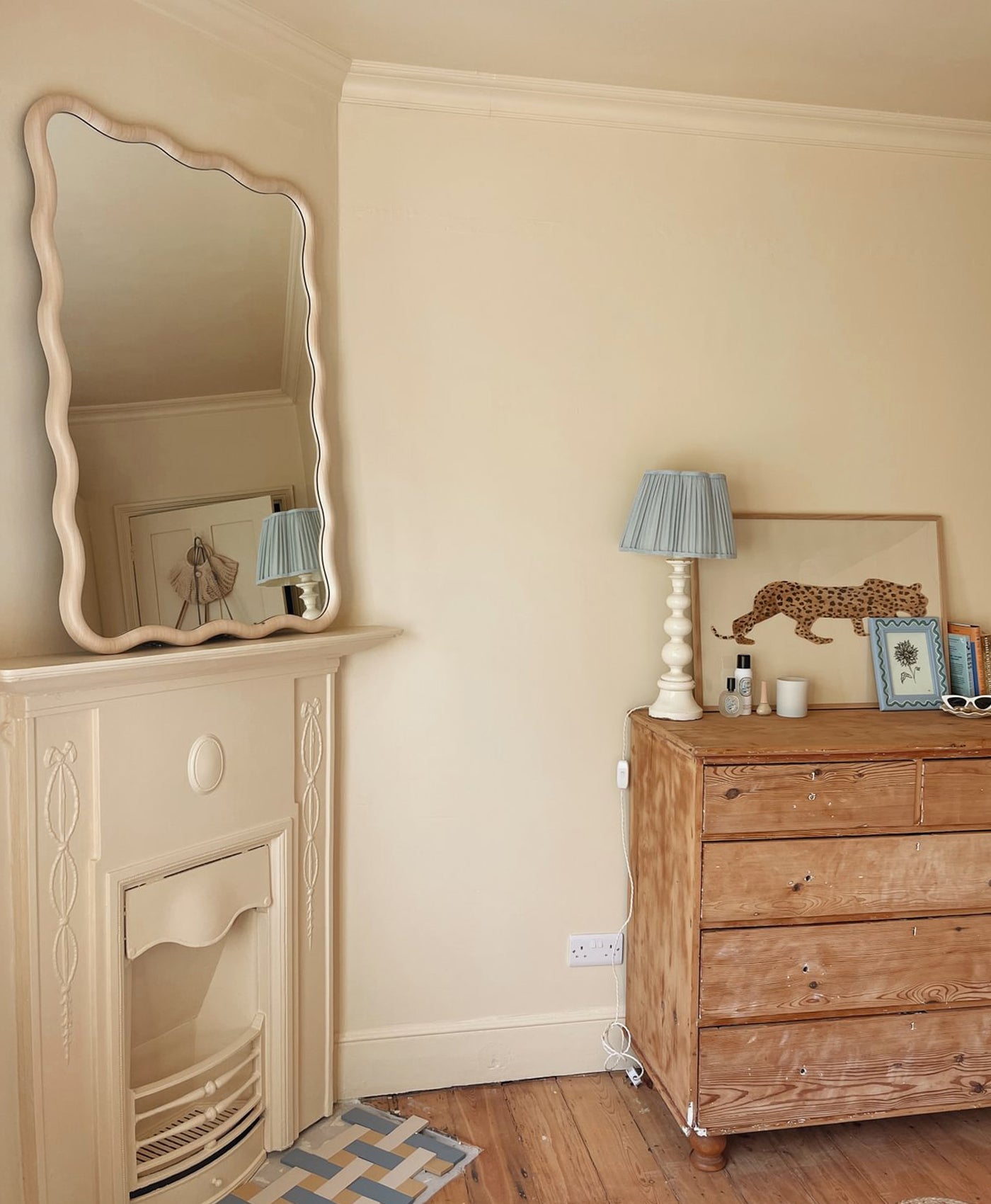 Room interior with a fireplace, mirror, wooden dresser, and decorative items, walls painted in warm cream paint