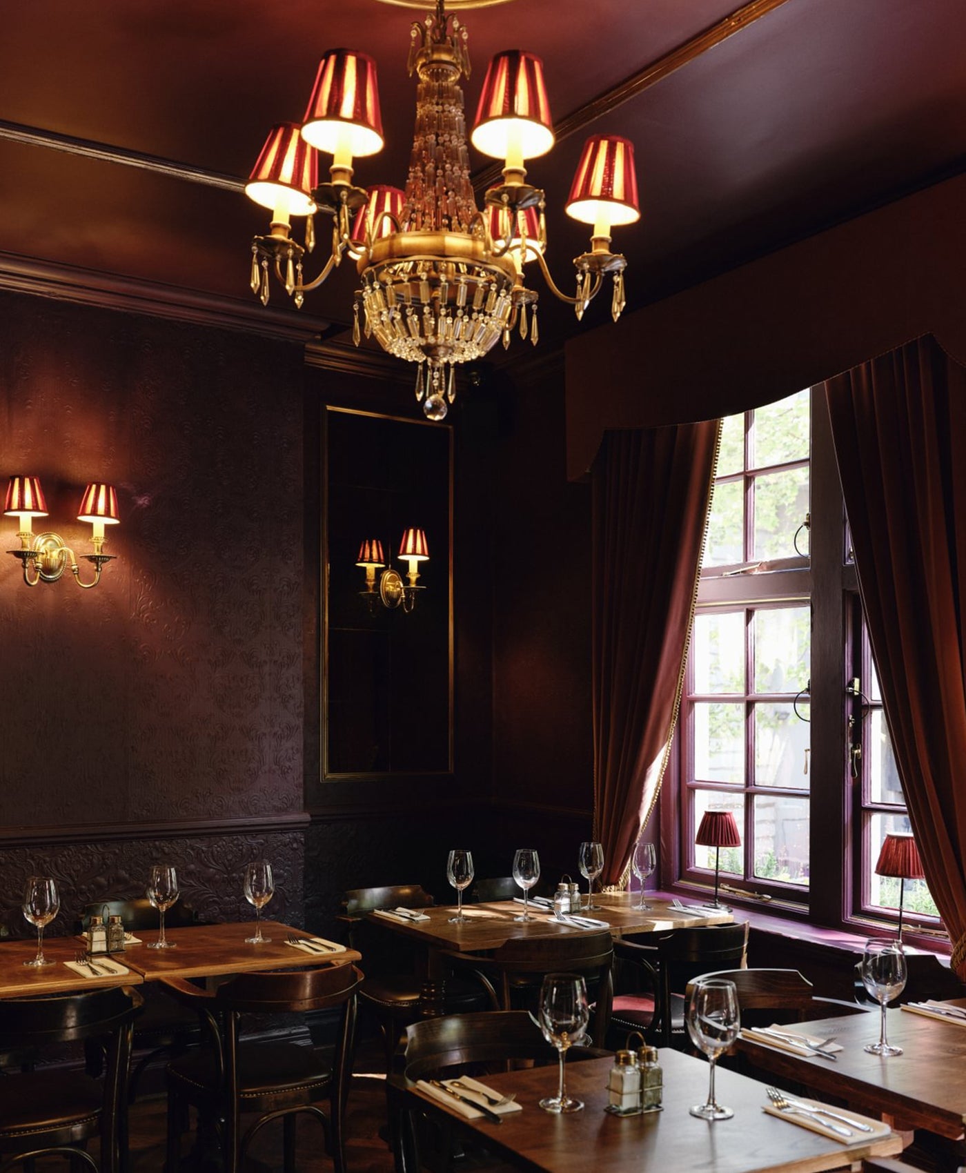 Luxurious rich deep red interior of a restaurant with a chandelier, tables, and wine glasses.