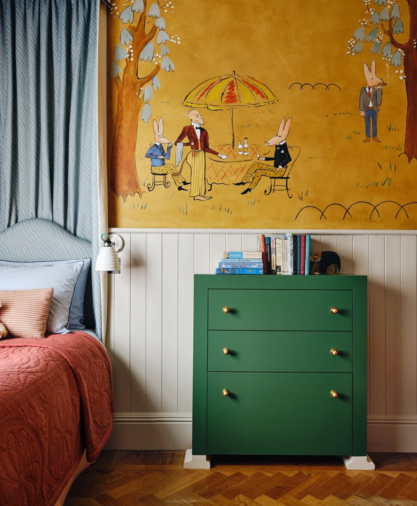 Green dresser against a wall with a colorful mural of rabbits at a table.