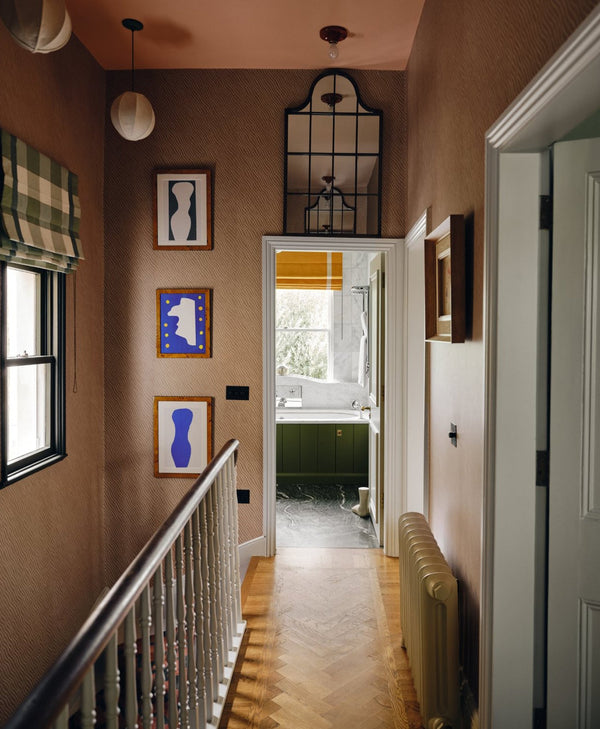 Hallway with staircase, framed art on walls, and a door leading to another room.