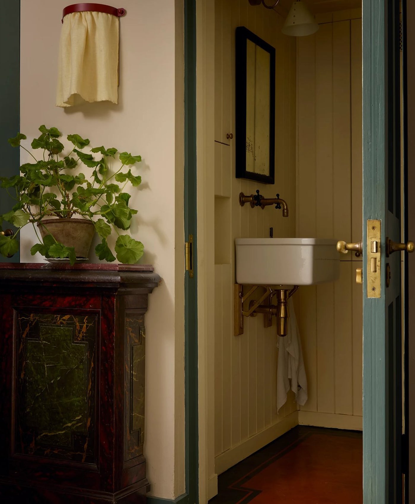 Bathroom interior painted in butter yellow with terracotta red floor and dusty teal coloured door