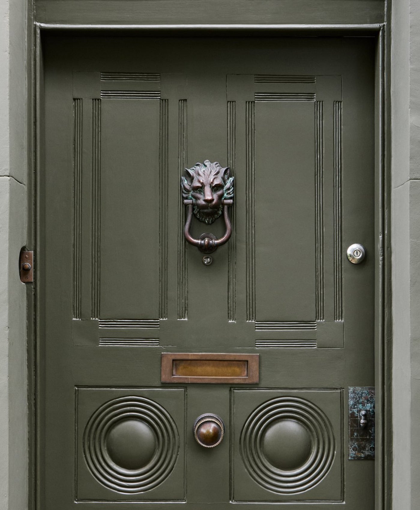 Olive green door with a lion head knocker and mail slot.