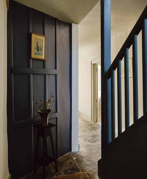 Narrow hallway with dark blue wooden wall panelling, a small table with a plant, and a staircase.