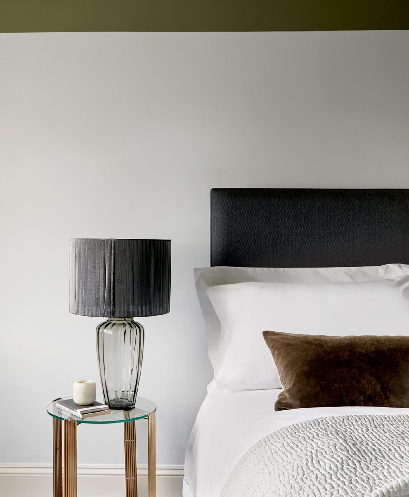 Modern bedroom with a bed, nightstand, and lamp against a greenish white wall.