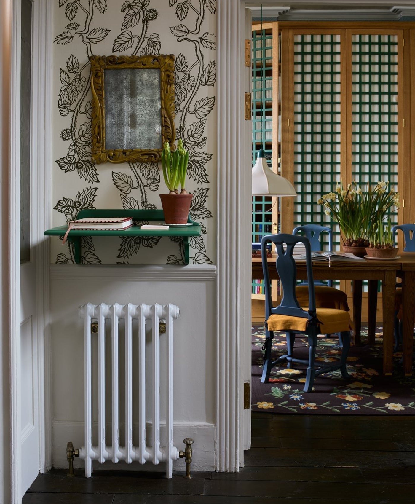 Nook with white radiator, green shelf, and decorative mirror on floral wallpaper.