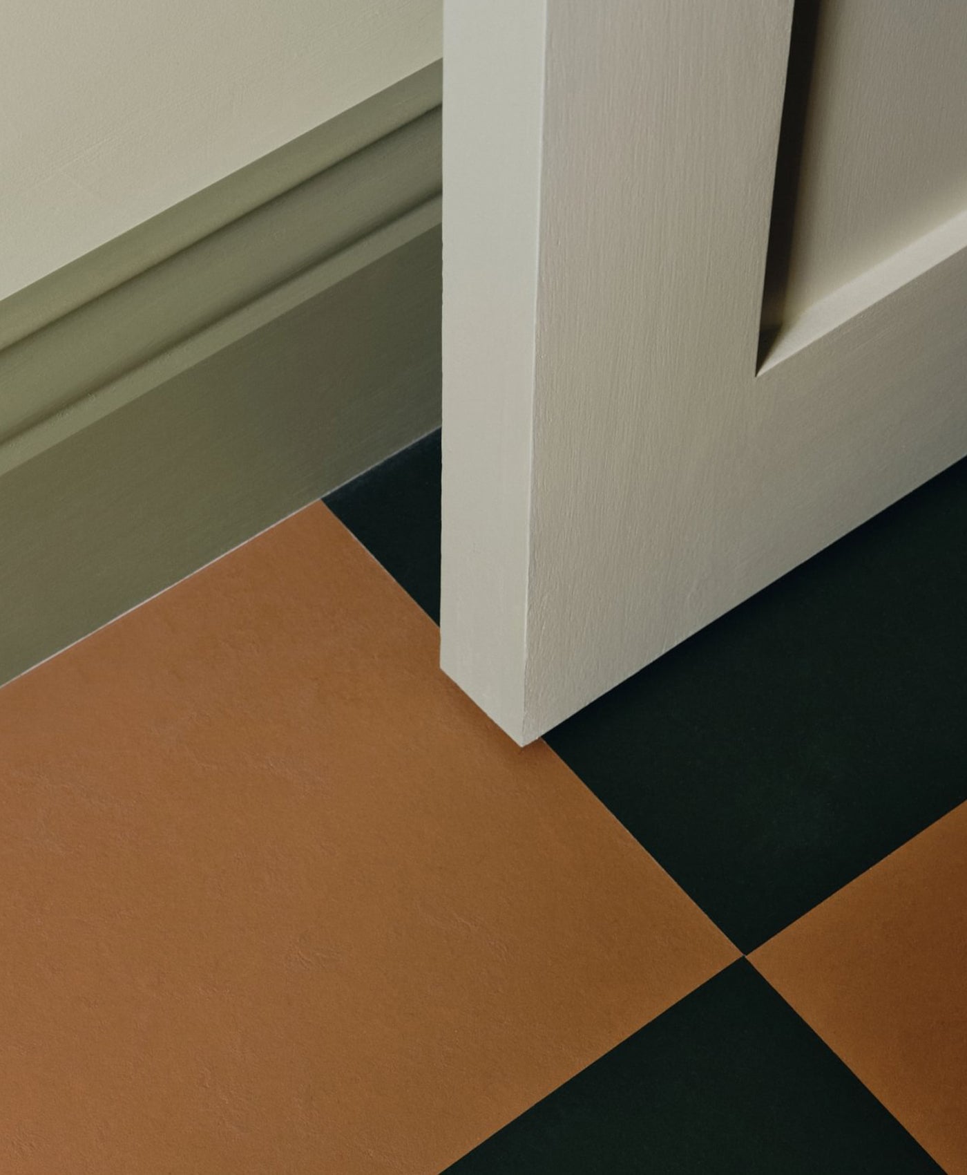 Close-up of a corner with a sage green woodwork and brown and black tiles.