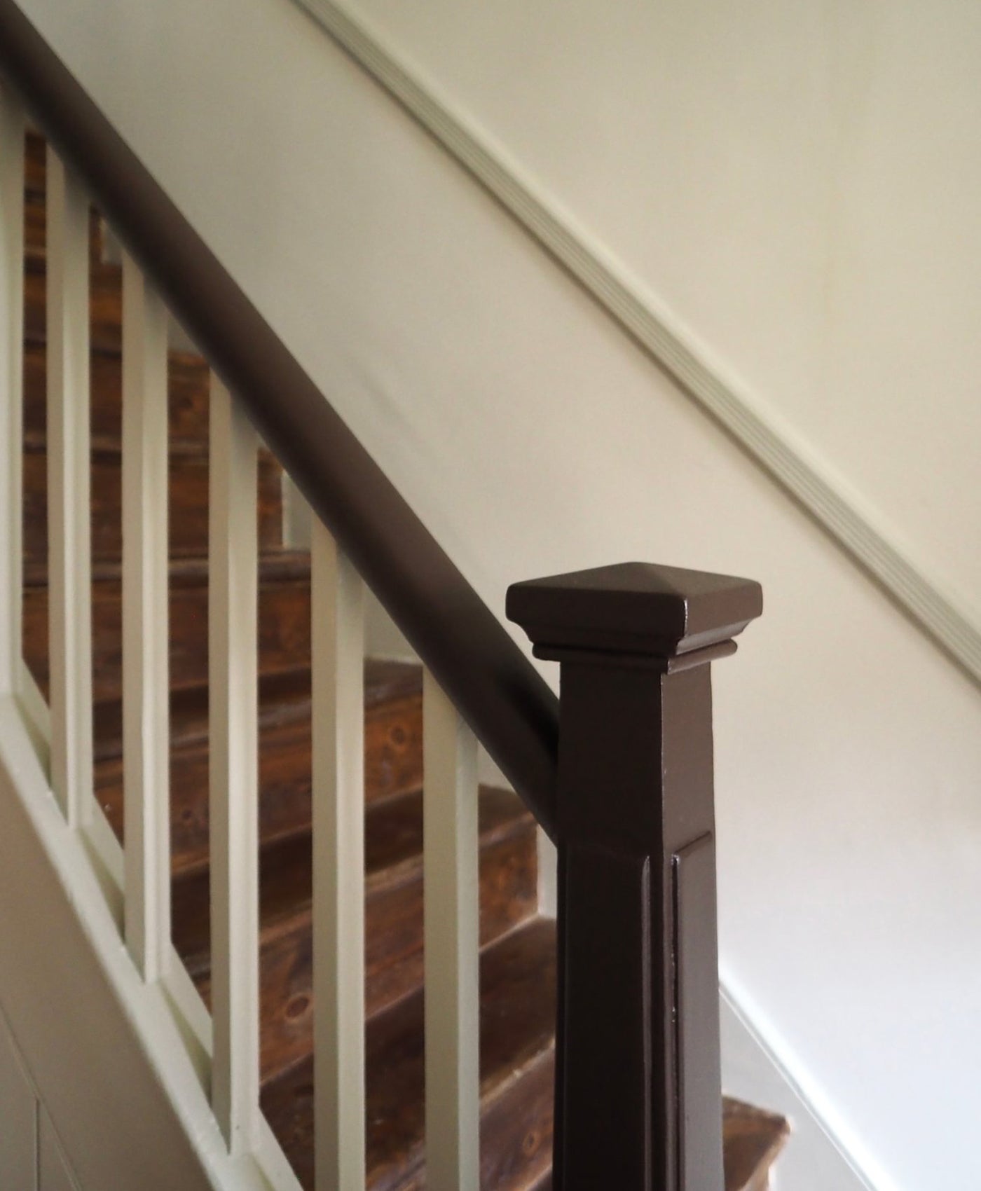 Wooden staircase with dark brown balusters and white spindles against a light wall.