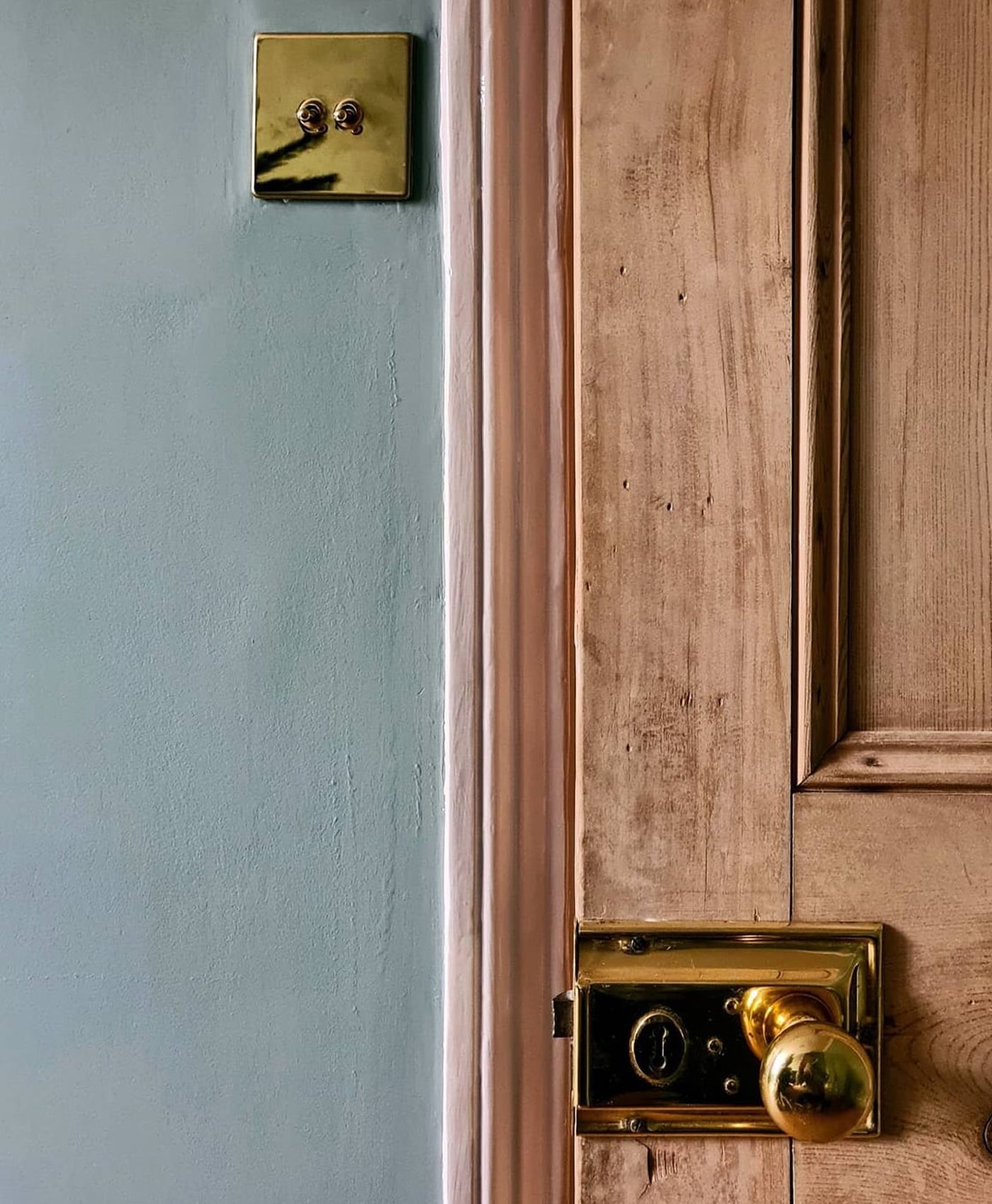 Close-up of a wooden door with brass doorknob and lock against a sage green wall.