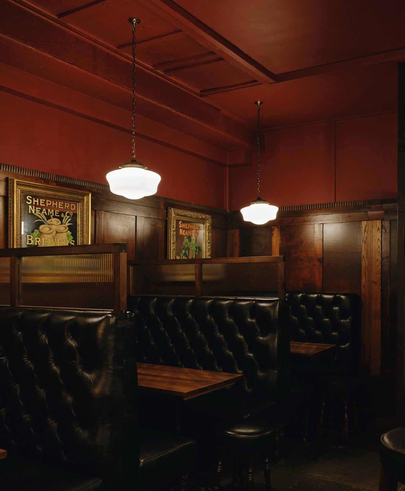 Dark red interior of a bar with leather booths and framed pictures on the wall.