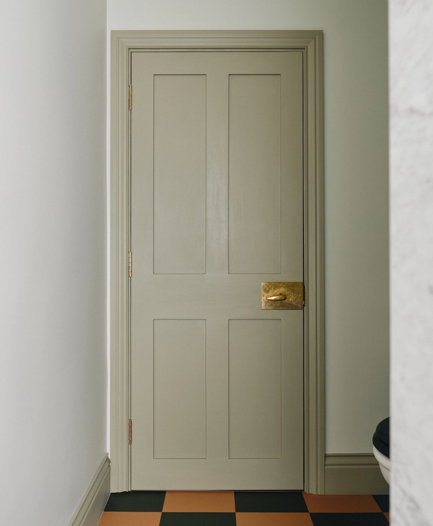 Sage green door with a gold handle on a light green wall with a checkered floor.