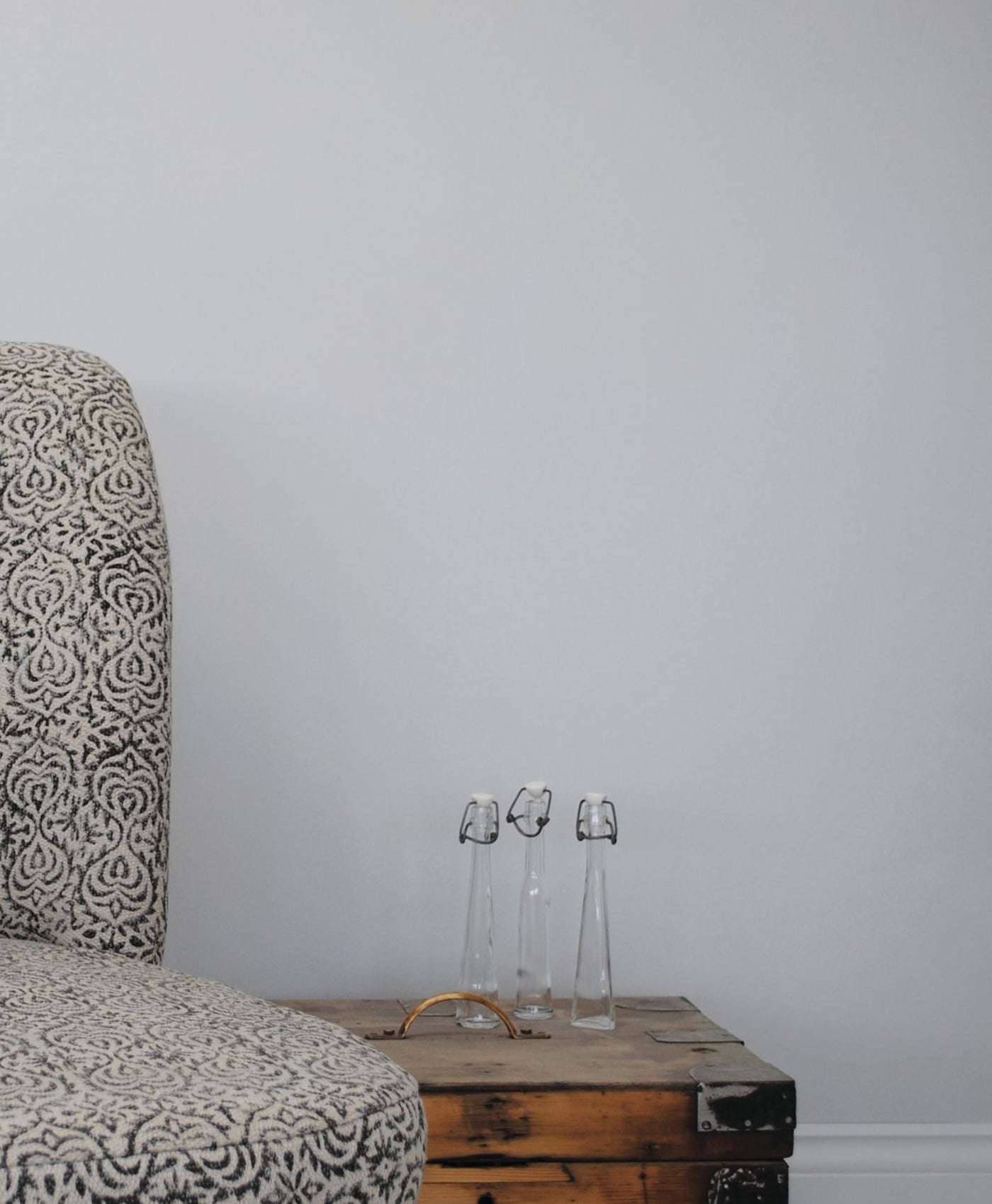 Patterned chair next to a wooden chest with two glass bottles on a blue grey wall background