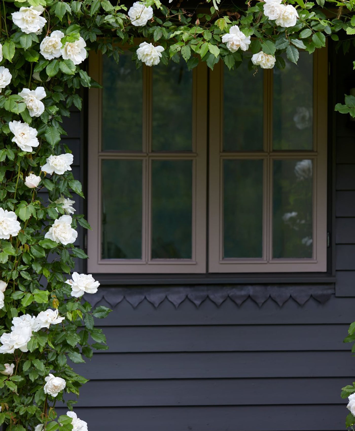 Window with white flowers and greenery on a dark painted wooden building