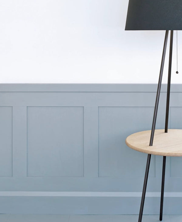 Modern floor lamp with black shade and wooden base against cool white painted wall with light blue panelling.