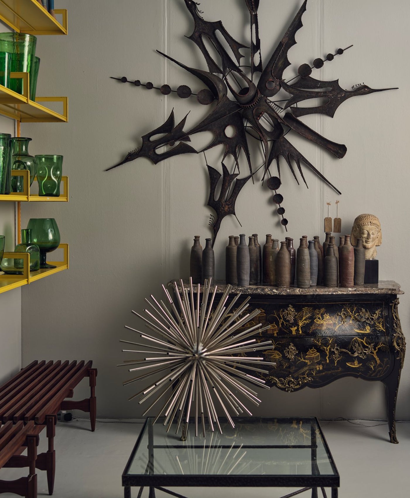 Grey interior with metal wall art, shelves with green vases, and a console table.