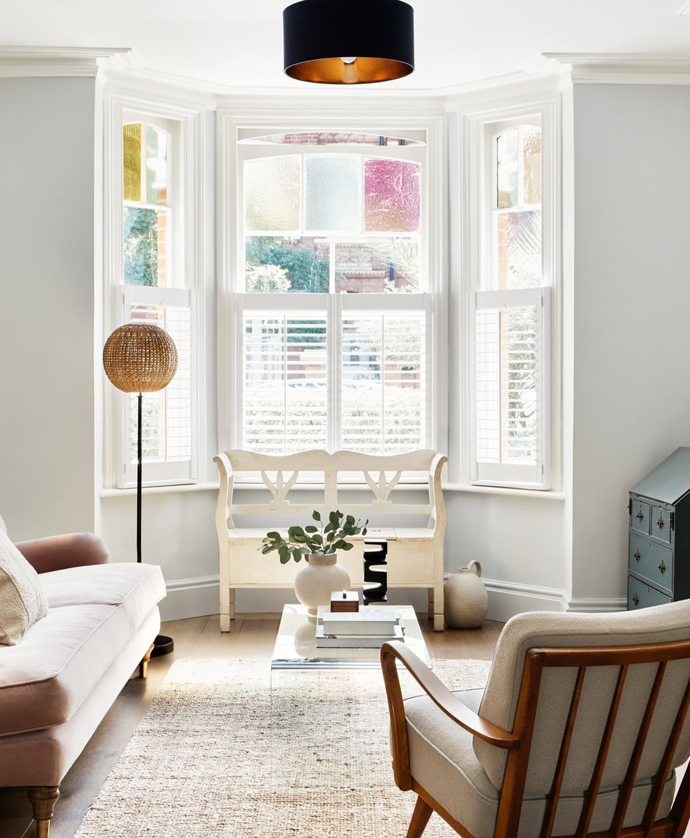 Living room in victorian house with bay window, painted in a light grey paint with white window shutters