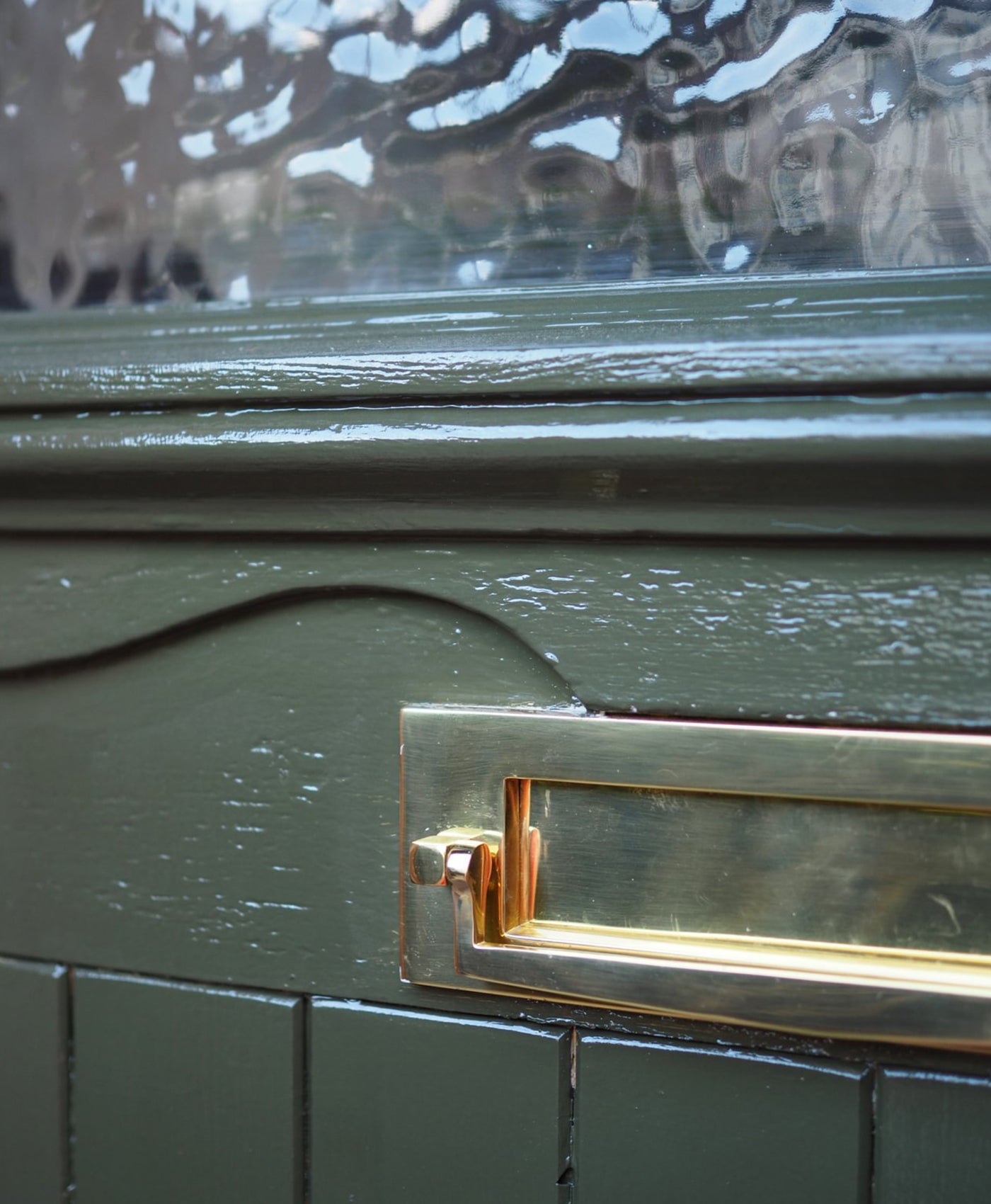 Close-up of a dark olive green front door with a gold handle