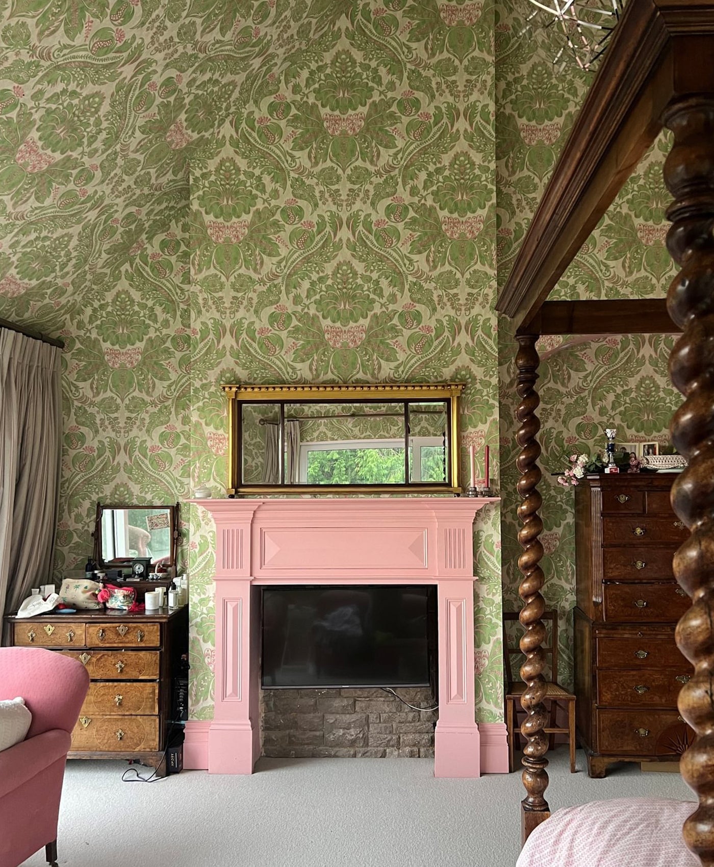 Vintage room with green patterned wallpaper, pink fireplace, and wooden furniture.