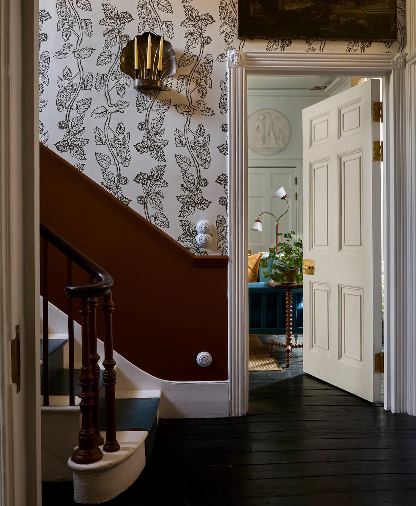 Staircase with decorative wall paper a terracotta brown wall with a white door opening to another room.