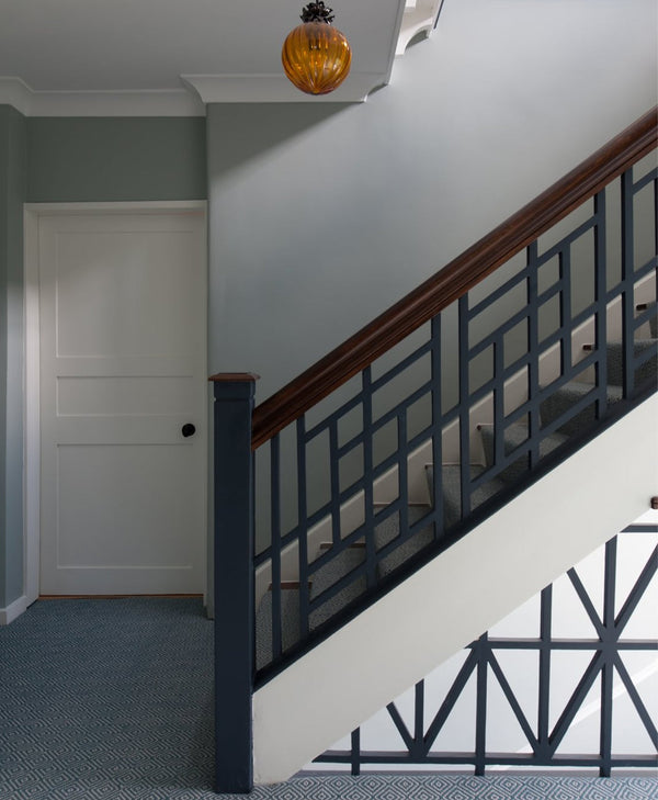 Green hallway, staircase with wooden handrail and metal railing in a home interior.