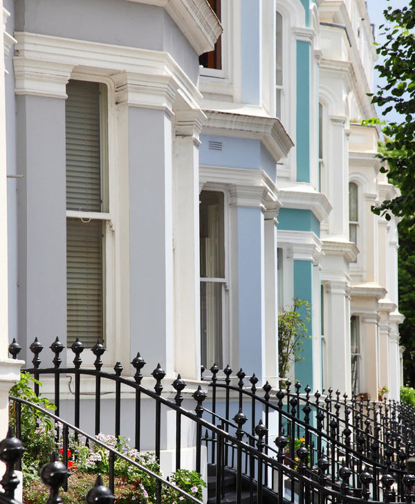 Row of houses painted light bliue, lilac, green blue and white, with a black metal fence in the foreground