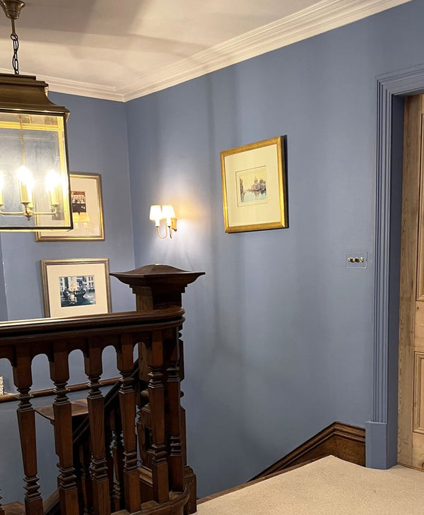 Staircase with wooden railings and framed pictures on a mid blue wall.