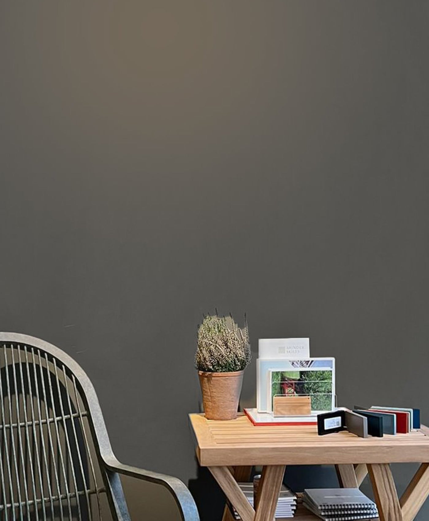 Minimalist office setup with a wooden desk, chair, and decorative items against a dark grey wall.