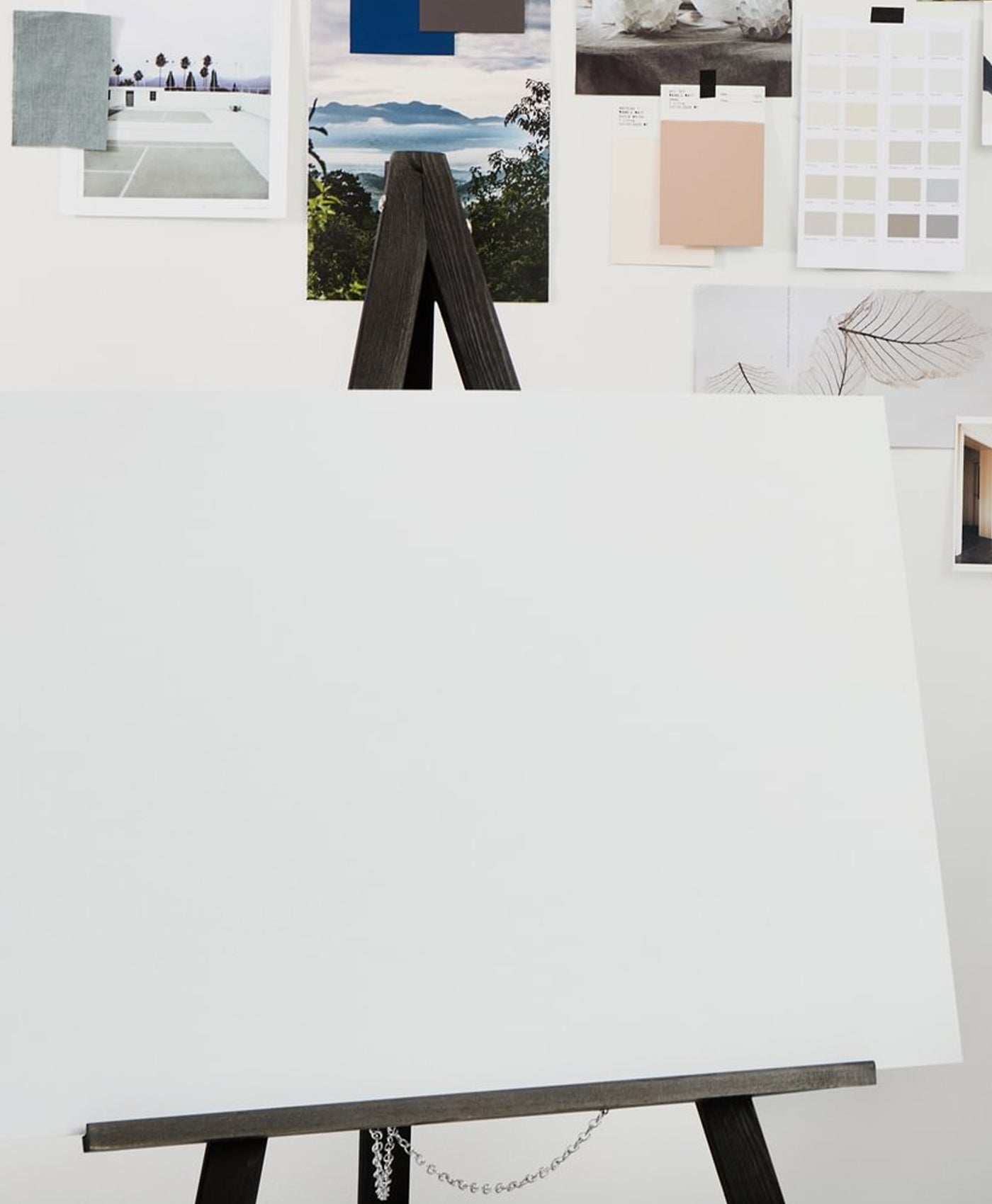 White canvas on an easel with a variety of color swatches and images displayed on a white wall.