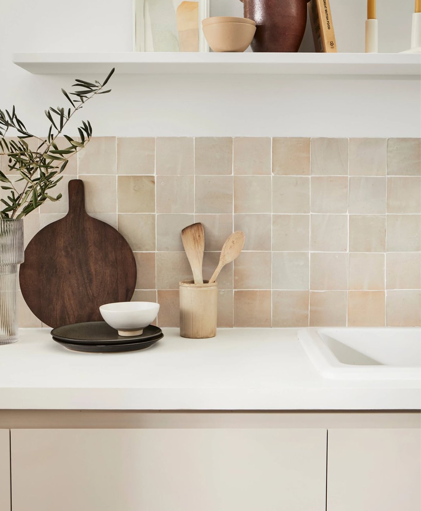 Kitchen counter with a tiled backsplash, wooden cutting board, and kitchen utensils, with white painted walls and neutral painted kitchen cabinets