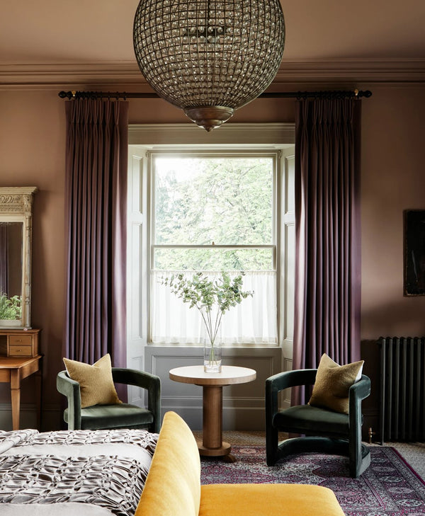 Plaster pink living room with purple curtains, a chandelier, and a round table.