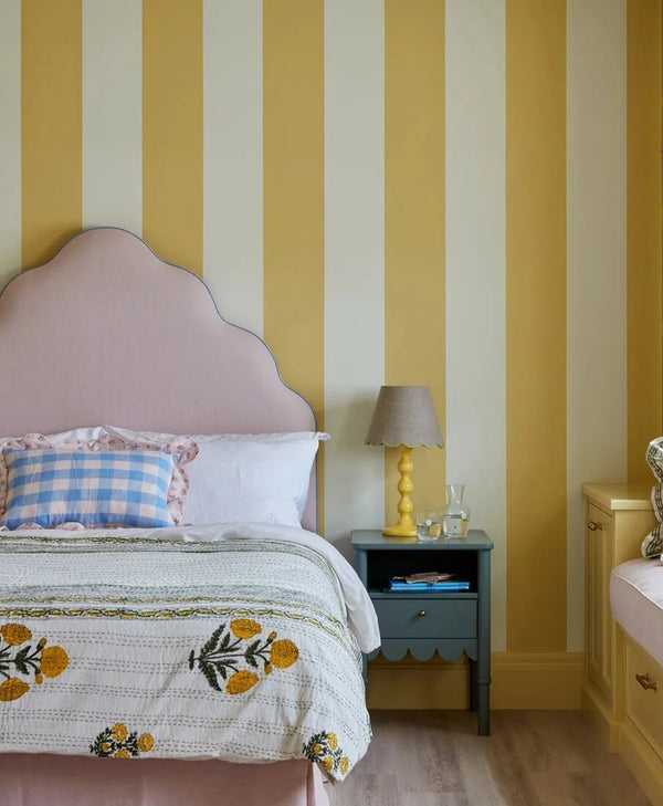 Bedroom with tonal yellow striped walls, pink headboard, and floral bedspread.