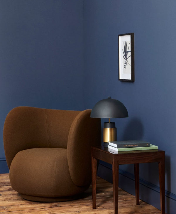 Brown armchair in a room with an indigo blue wall, side table, and framed artwork.