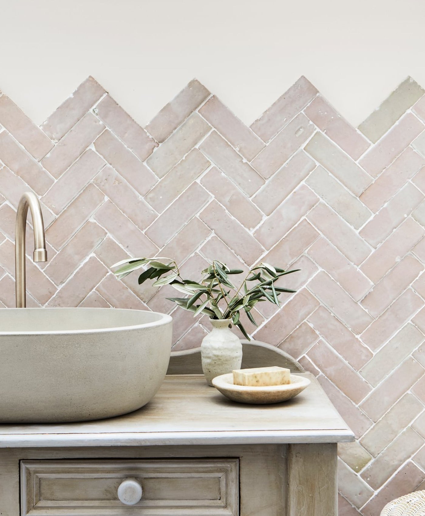 Bathroom vanity with a herringbone tile backsplash and pale pink painted wall