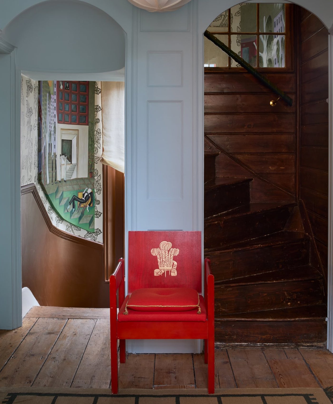Red chair with a gold design in a blue grey room with wooden floors and a staircase.