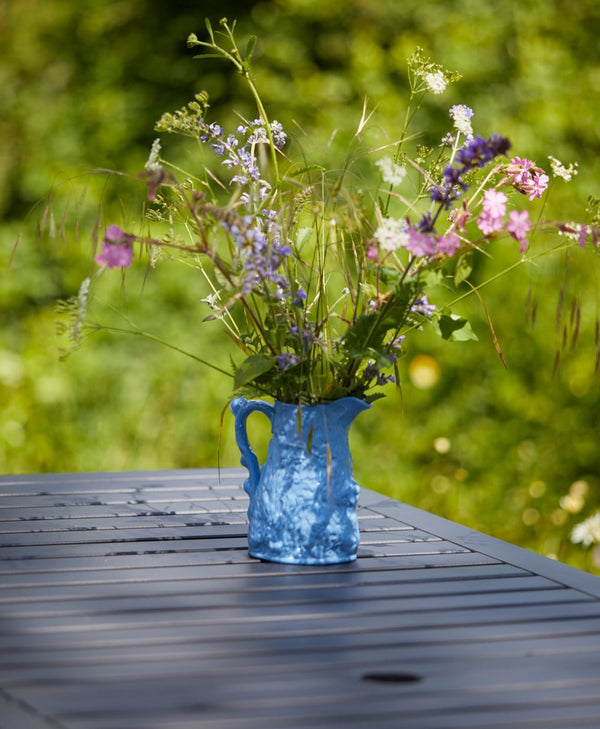 Blue ceramic vase with wildflowers on a wooden table painted in deep blue outdoors