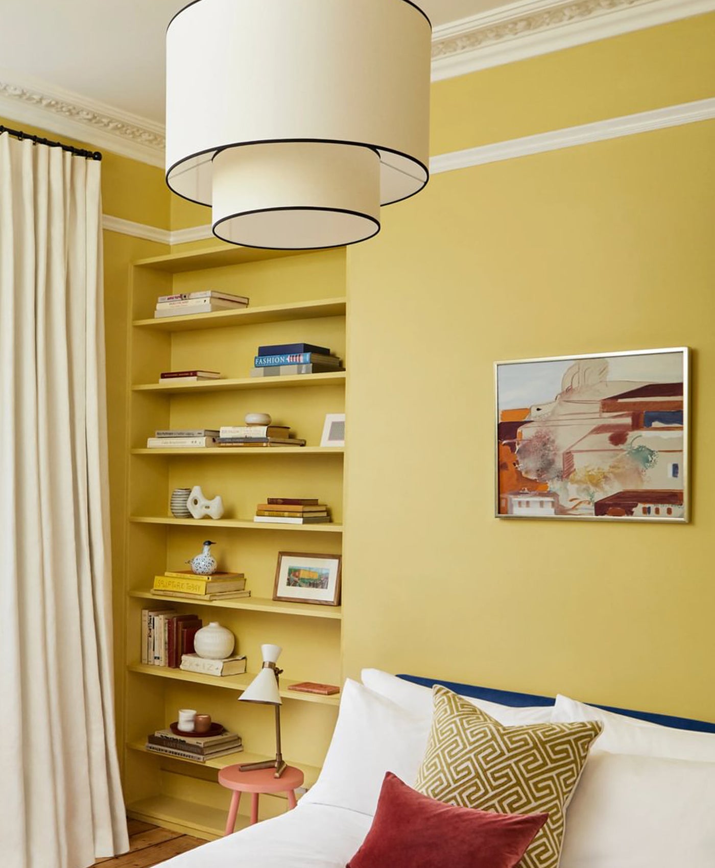 Living room with yellow walls, bookshelf, and a bed with pillows.
