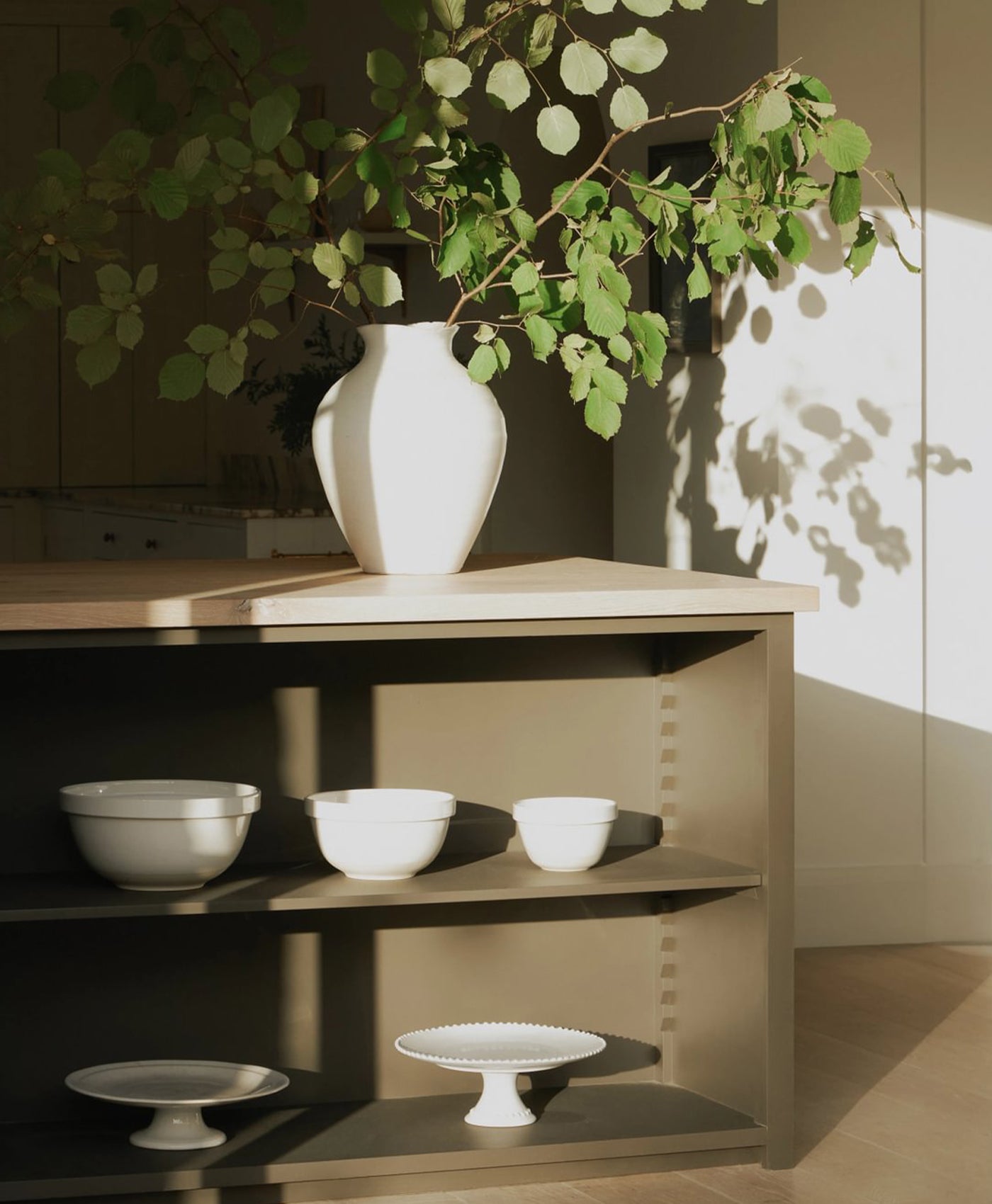 White vase on a wooden shelf with bowls and a plant, in kitchen island painted in green brown paint