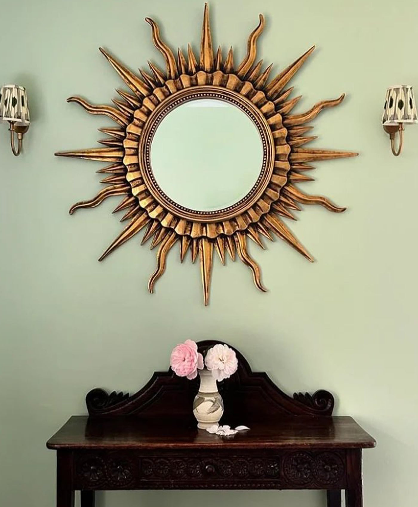 Decorative sun-shaped mirror on a light green wall with a wooden console table below.