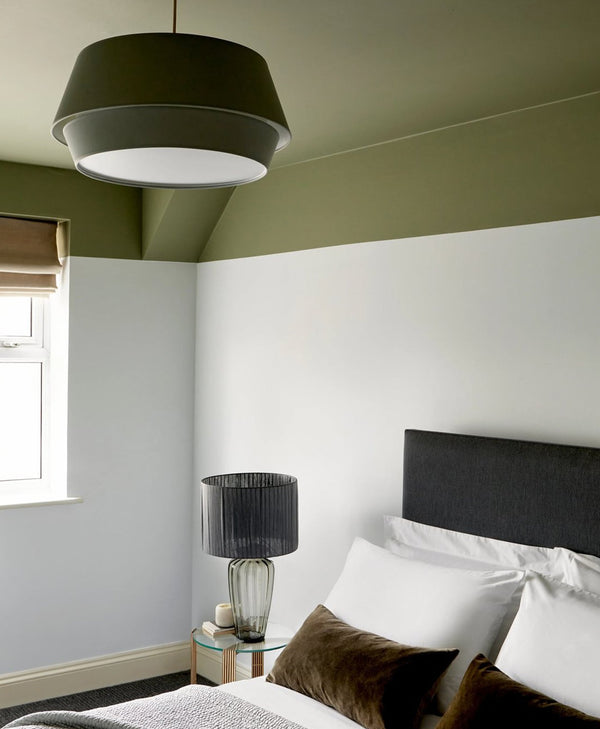 Modern bedroom with green walls, a bed with white pillows, and a black pendant light.