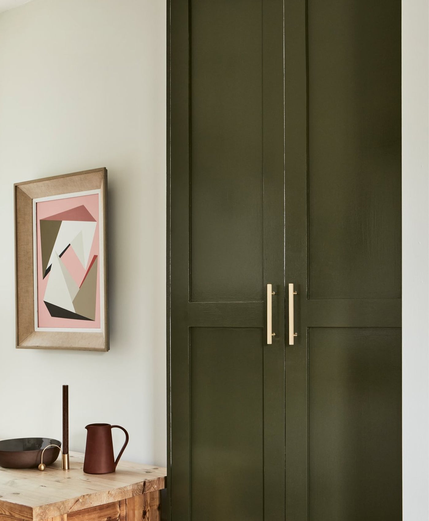 Olive green cabinet with gold handles next to a wall with abstract art and decor items.