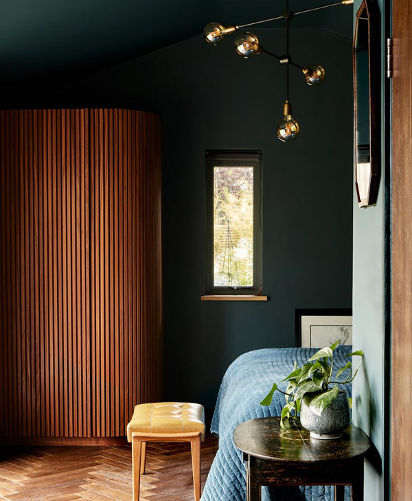 Modern bedroom with dark walls, wooden floor, and decorative lighting fixture.
