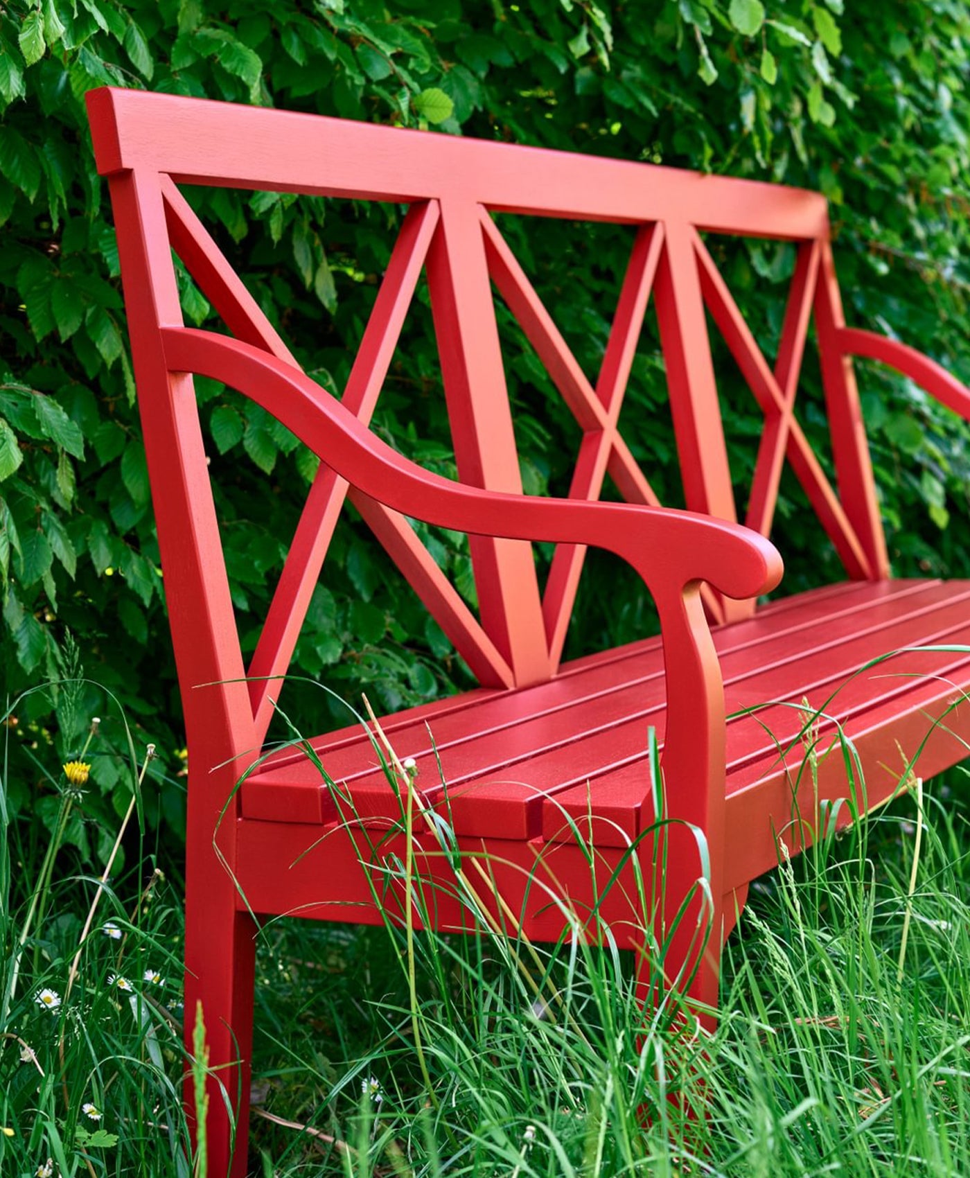 Red bench in a grassy area with green foliage