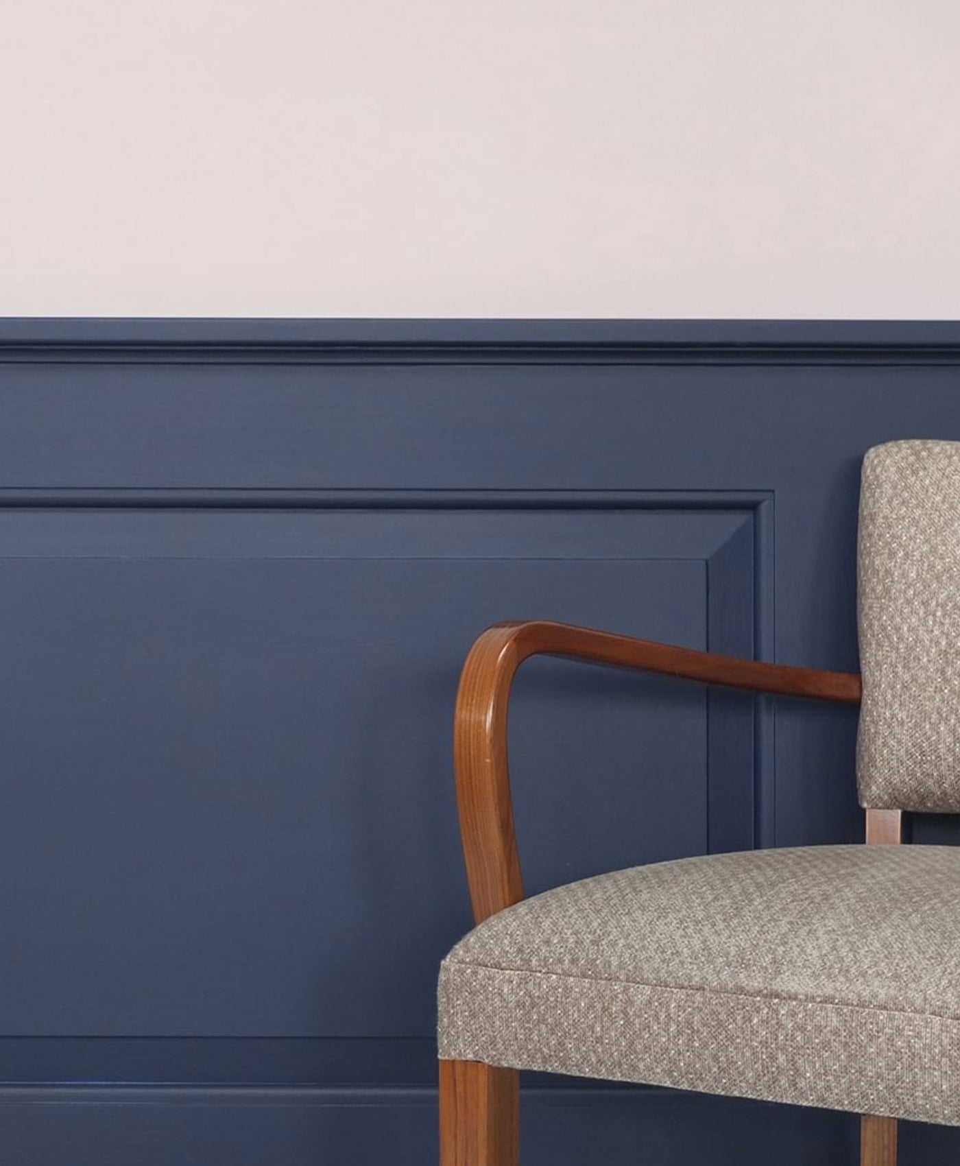 Chair with wooden armrest against a blue panelled wall with a light grey paint at the top