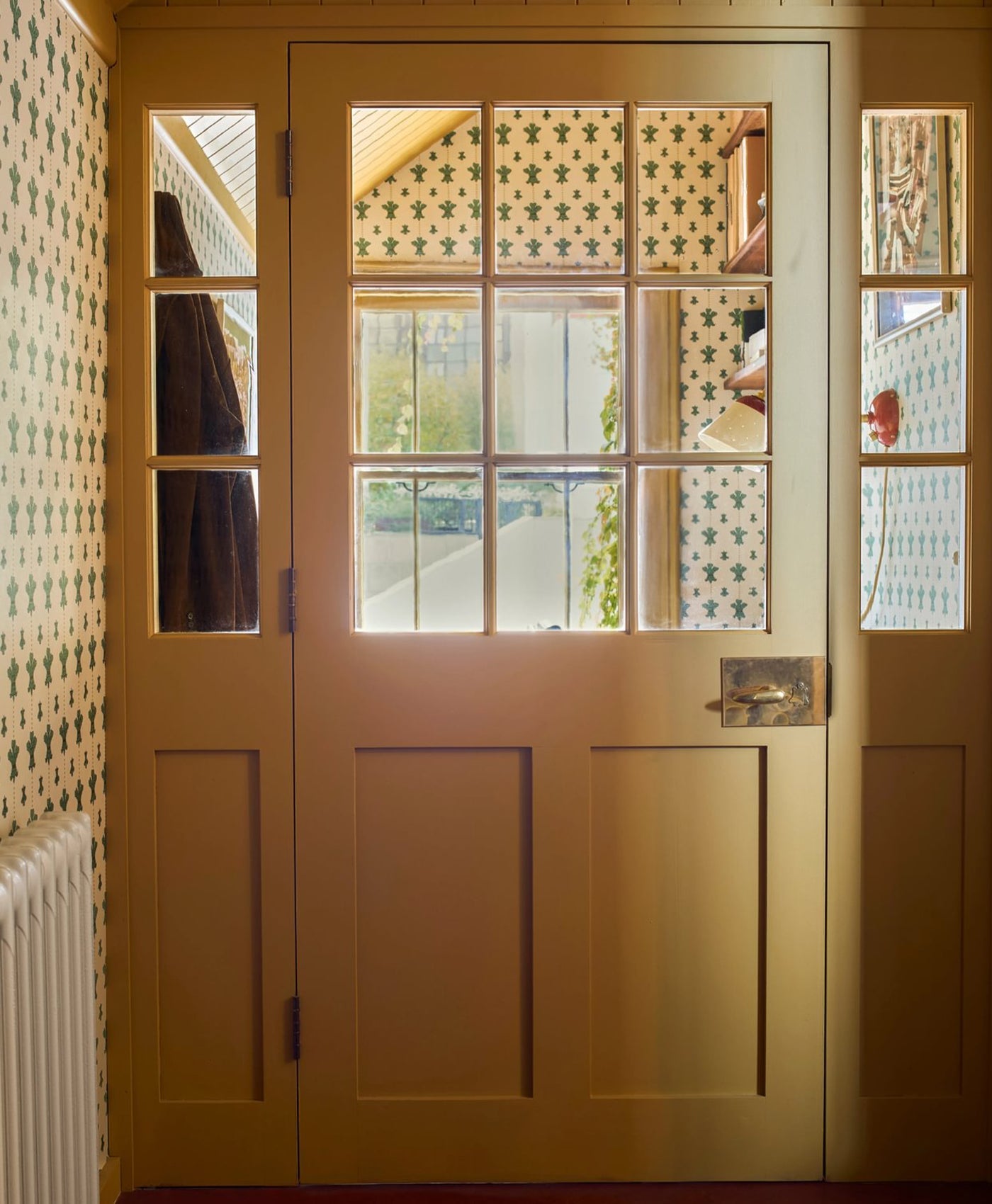 butter yellow door with glass panels in a room with patterned wallpaper.