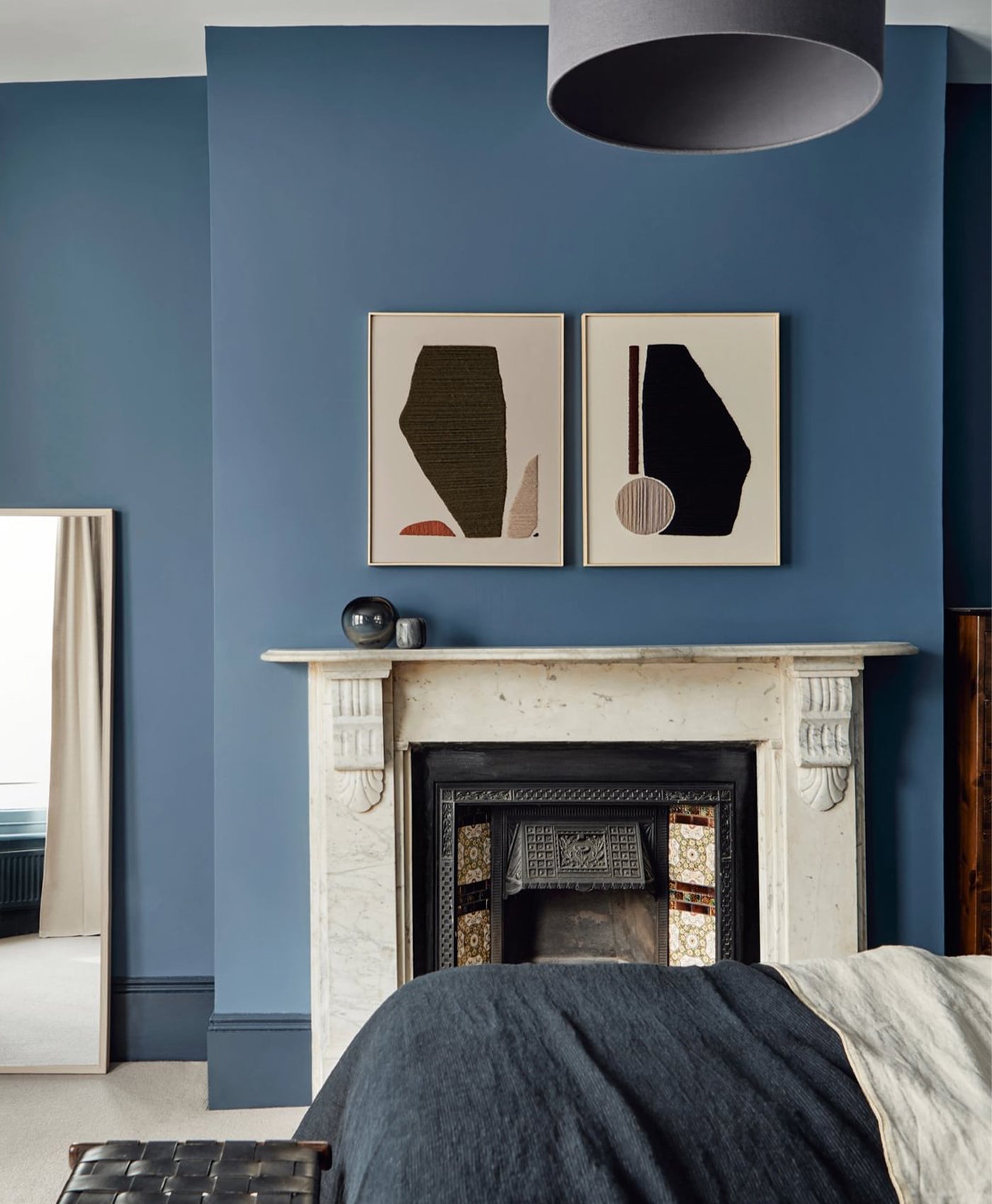 marine blue wall with abstract art above a fireplace in a bedroom.
