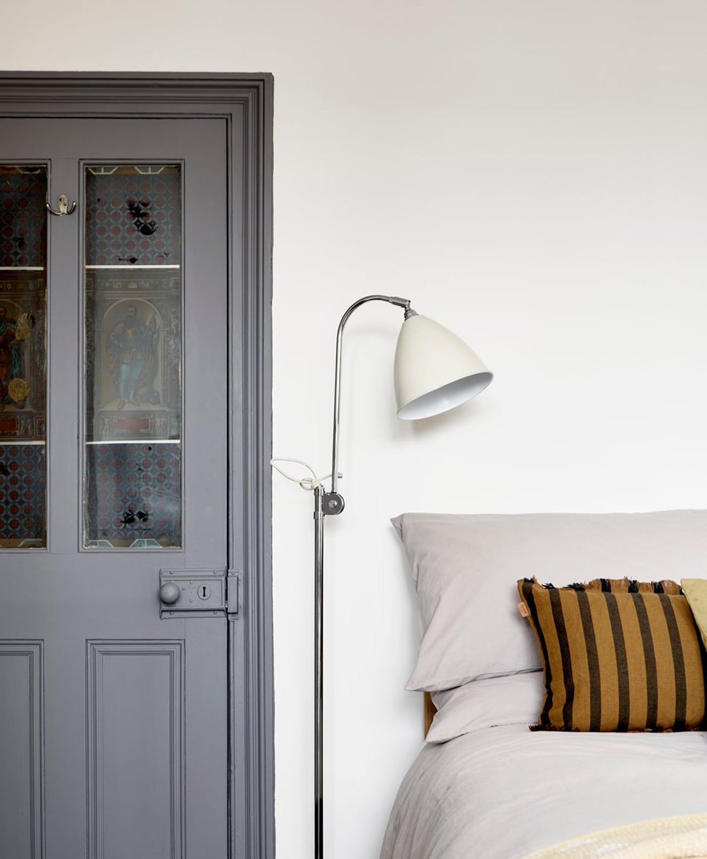 Grey door with glass panels in a light pink bedroom setting with a bed and lamp.